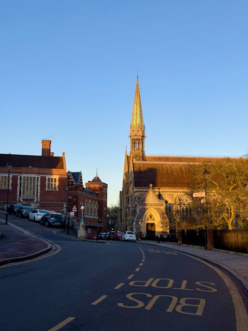 A street scene in an urban area with a mix of commercial and religious buildings, featuring a prominent historic church with a large rose window and pointed arch entrance at the end of the street. The